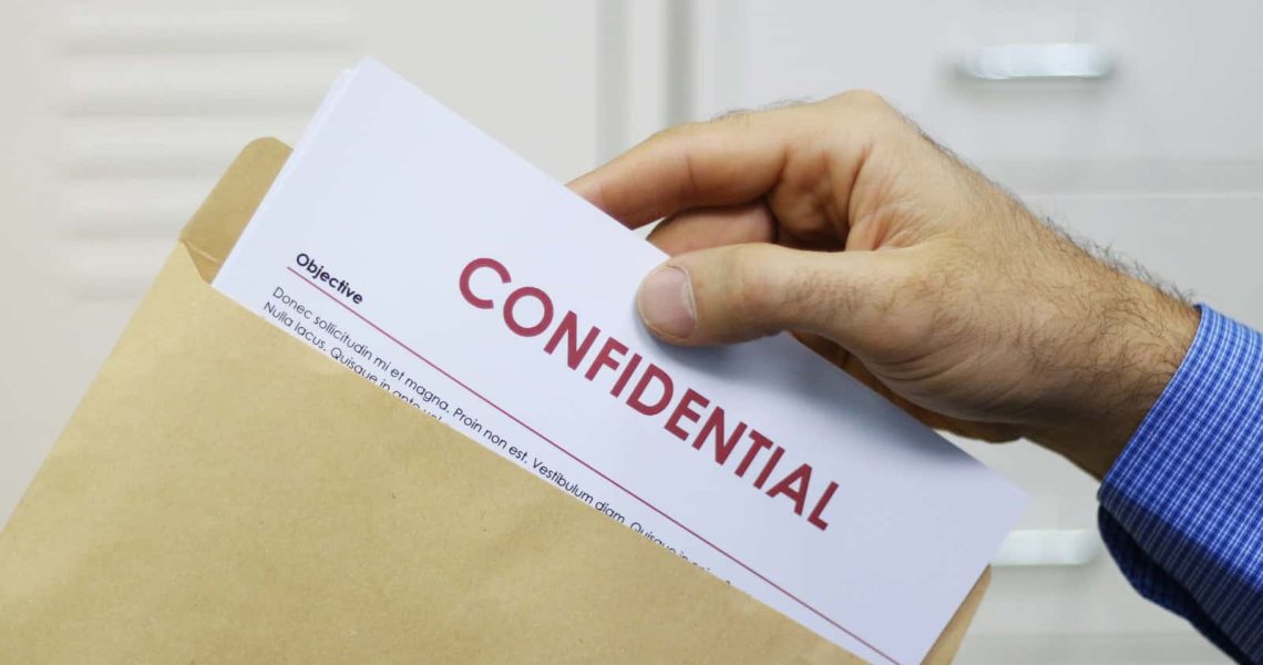 Cropped view image of a man handling confidential documents placing them inside a brown manilla envelope for mailing
