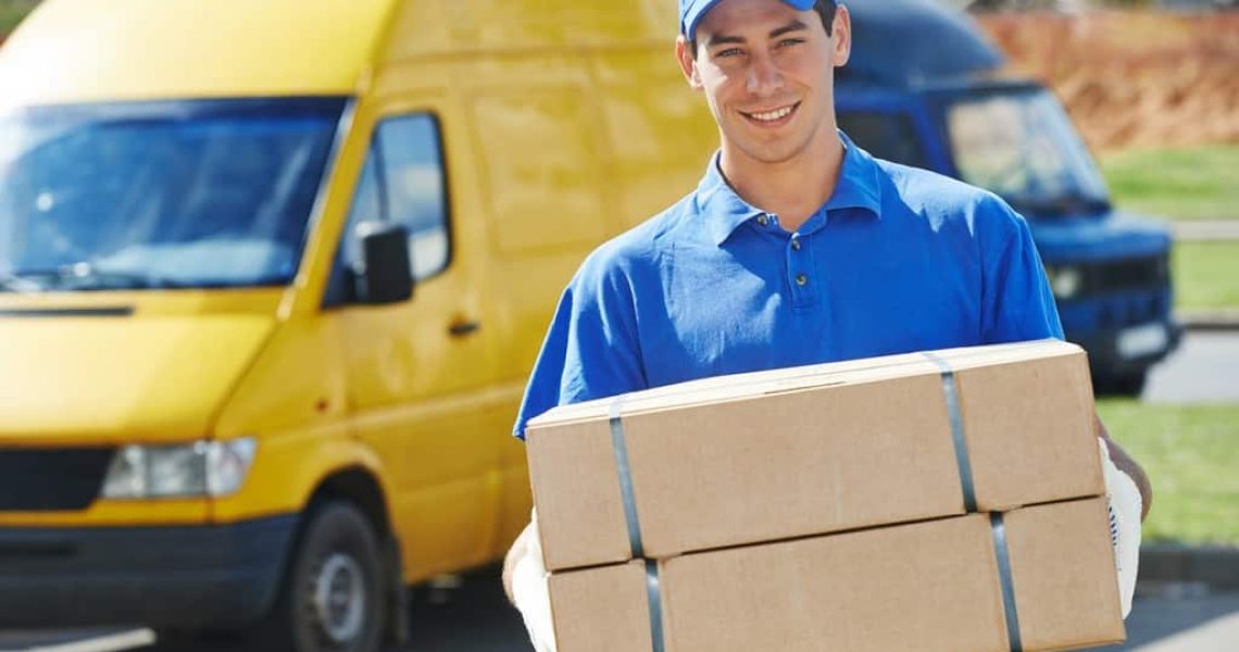 Smiling young male postal delivery courier man in front of cargo van delivering package